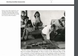 Zdjęcie w formie wycinka z gazety na którym znajdują się ludzie oglądający grafiki ułożone na podłodze. Zdjęcie czarno białe.