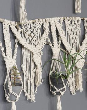 na szarej ścianie, jasna makrama, w niej szare osłonki z roślinami