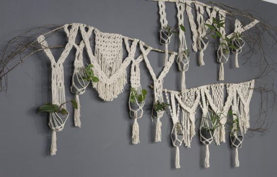 na szarej ścianie, jasna makrama, w niej szare osłonki z roślinami