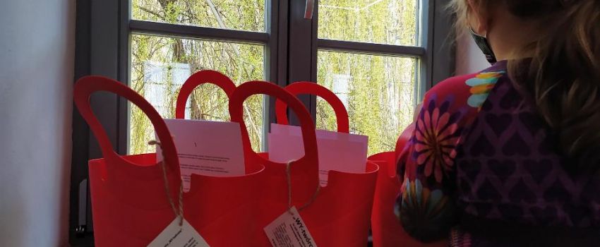 Na parapecie stoją cztery czerwone plastikowe kosze z materiałami plastycznymi. Dziewczynka sięga po jeden z nich.