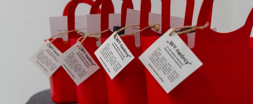 Na tle białej ściany stoją cztery czerwone plastikowe kosze. W nich materiały plastyczne