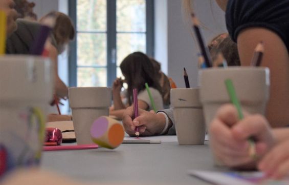 Sala warsztatowa. Dzieci rysują kredkami. Po stole toczy się kolorowa kostka.