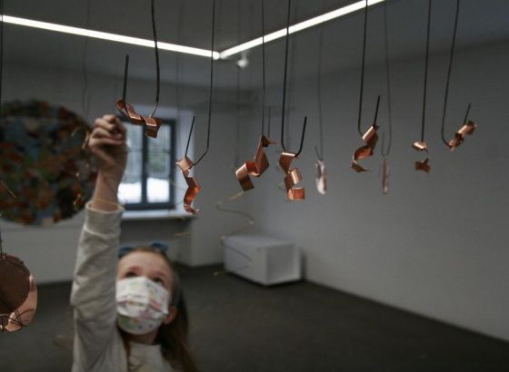 Sala warsztatowa Galerii Arsenał. Dziewczynka w maseczce sięga ręką do metalowej instalacji.