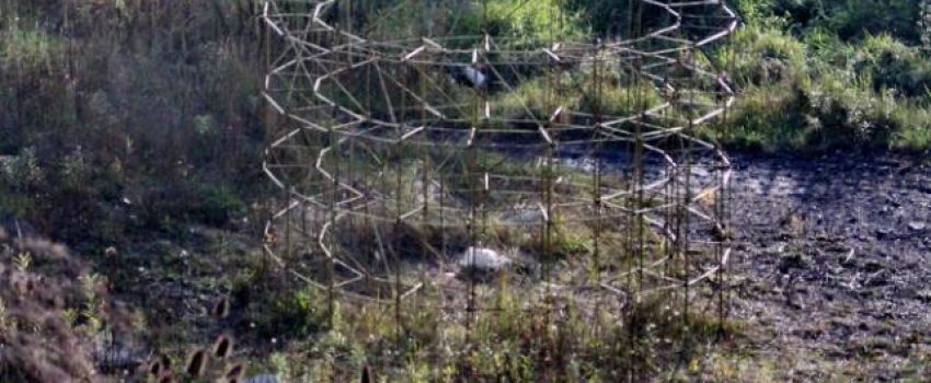 Instalacja znajdująca się na wolnym powietrzu. Ustawiona jest na terenie piaszczystym, porośniętym roślinami i trawami.