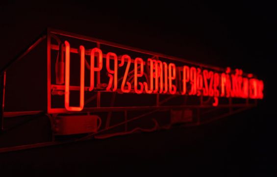 Napis w formie neonu. Kolor czerwony. Tło czarne.