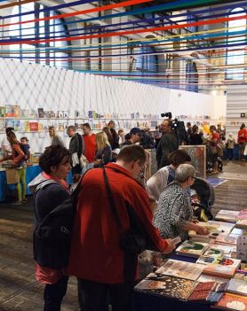 Duża hala ze stoiskami na których znajdują się książki. Ludzie zwiedzający Targi Książki w hali starej elektrowni w Białymstoku.