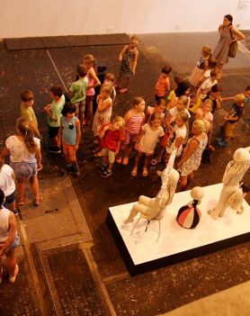W centrum zdjęcia grupa dzieci podczas warsztatów w hali elektrowni.