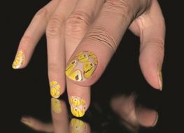 Zbliżenie na dłoń. Wyróżniają się paznokcie ozdobione żółtymi plamami i kropkami.