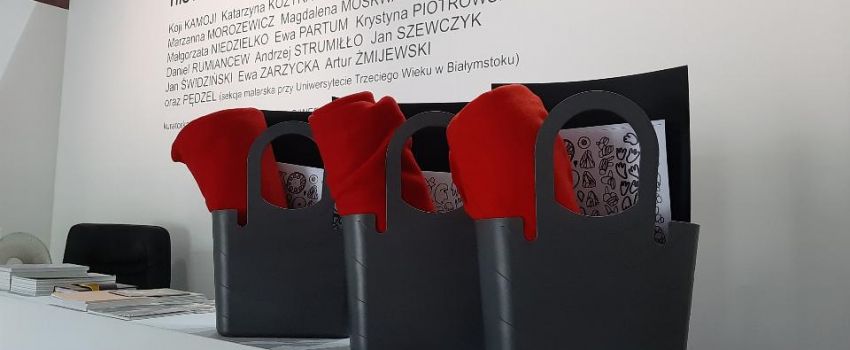 Działania twórcze "WY-twórcy" do wystawy Historie o starości. Torby z kocykami i zadaniami stojące na ladzie. W tle napis: tytuł wystawy, nazwiska artystów i kuratorki.