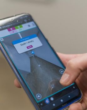 Dłoń trzymająca telefon z uruchomioną grą Seppo, w której widać mapę wystawy z obecnymi na niej dziełami sztuki