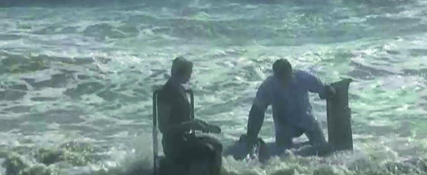 dwie osoby wychodzące z morza, próbujące usiąść na krzesłach